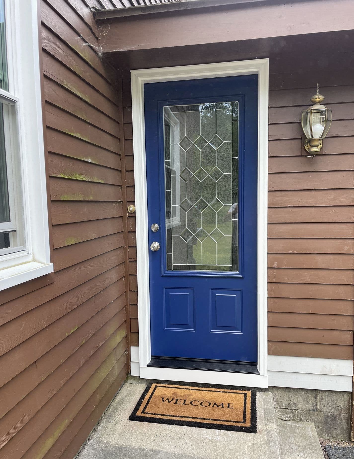 A royal blue entry door with large glass window on a brown house.