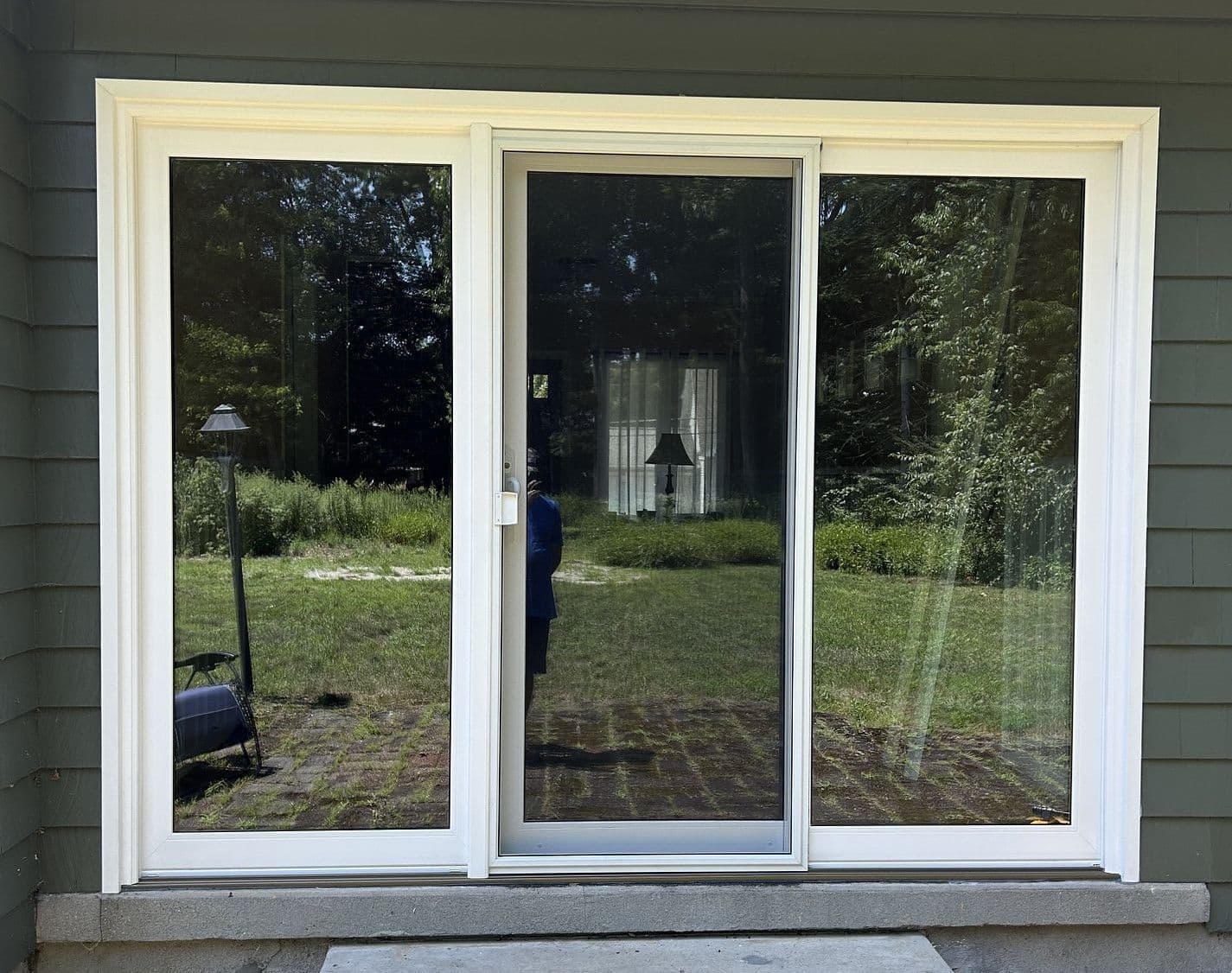 Three newly-installed sliding glass patio doors with white trim on a dark green house.