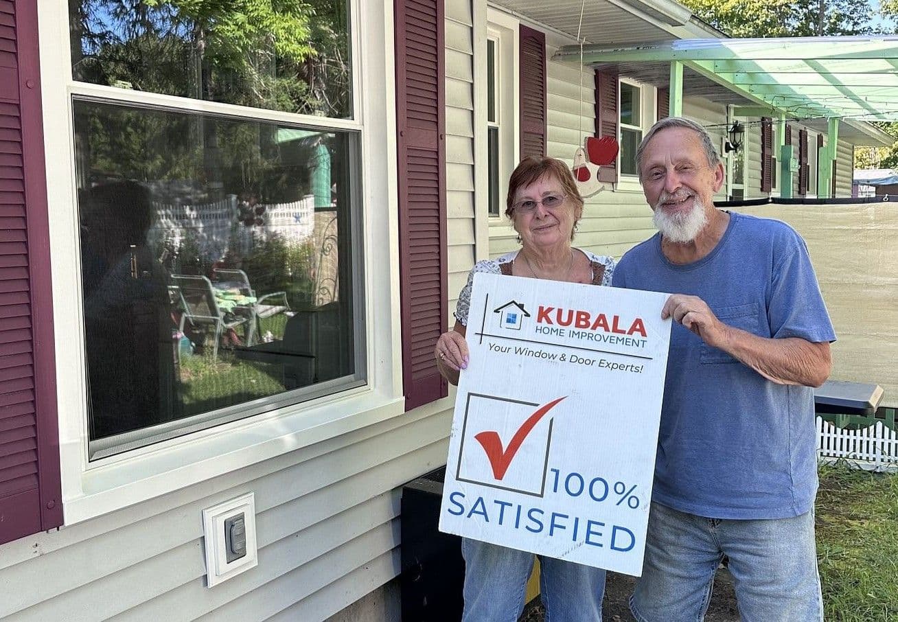 Homeowners hold a sign that reads "100% Satisfied" and stand in front of a newly-installed window.