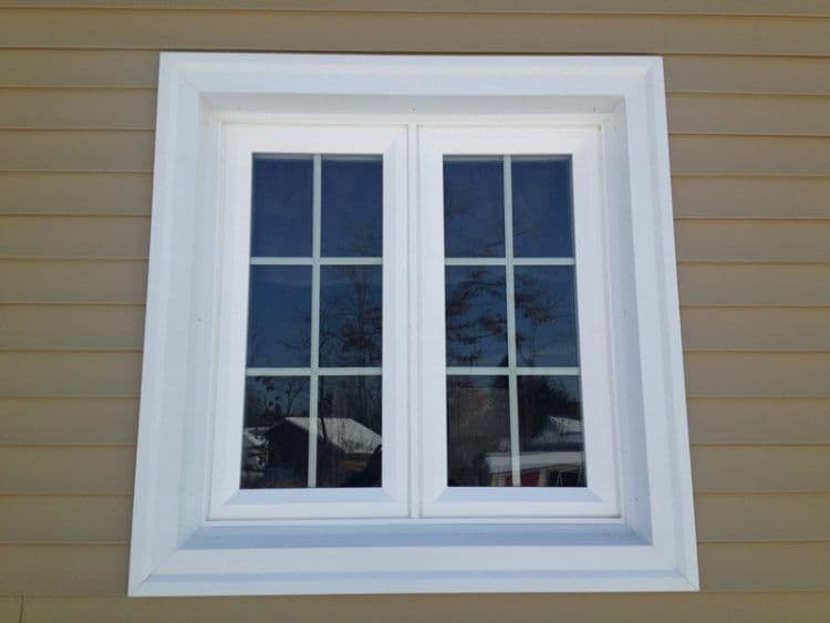 Newly-installed replacement window with white trim as viewed from the exterior of a tan house.