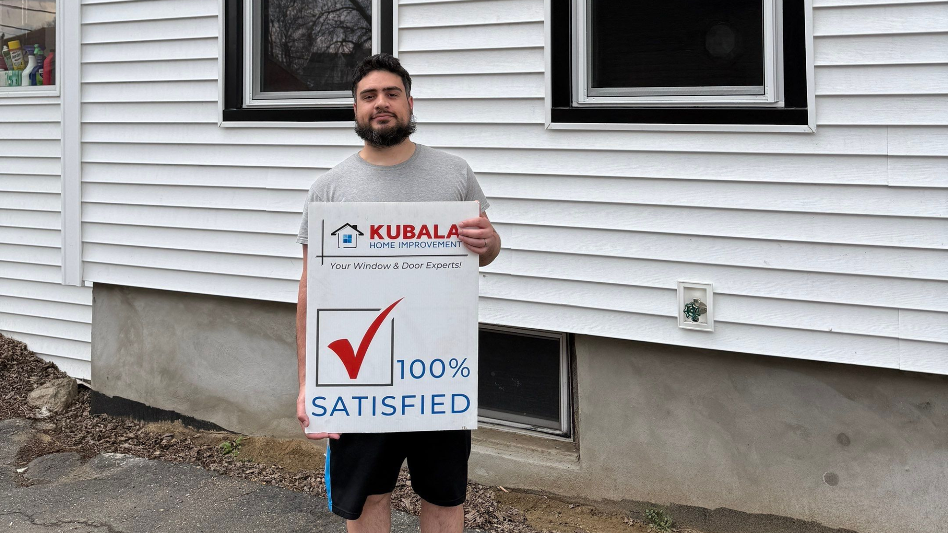 Picture of Octavio smiling and holding a "100% Satisfied" sign in front of his new windows in Springfield, MA.
