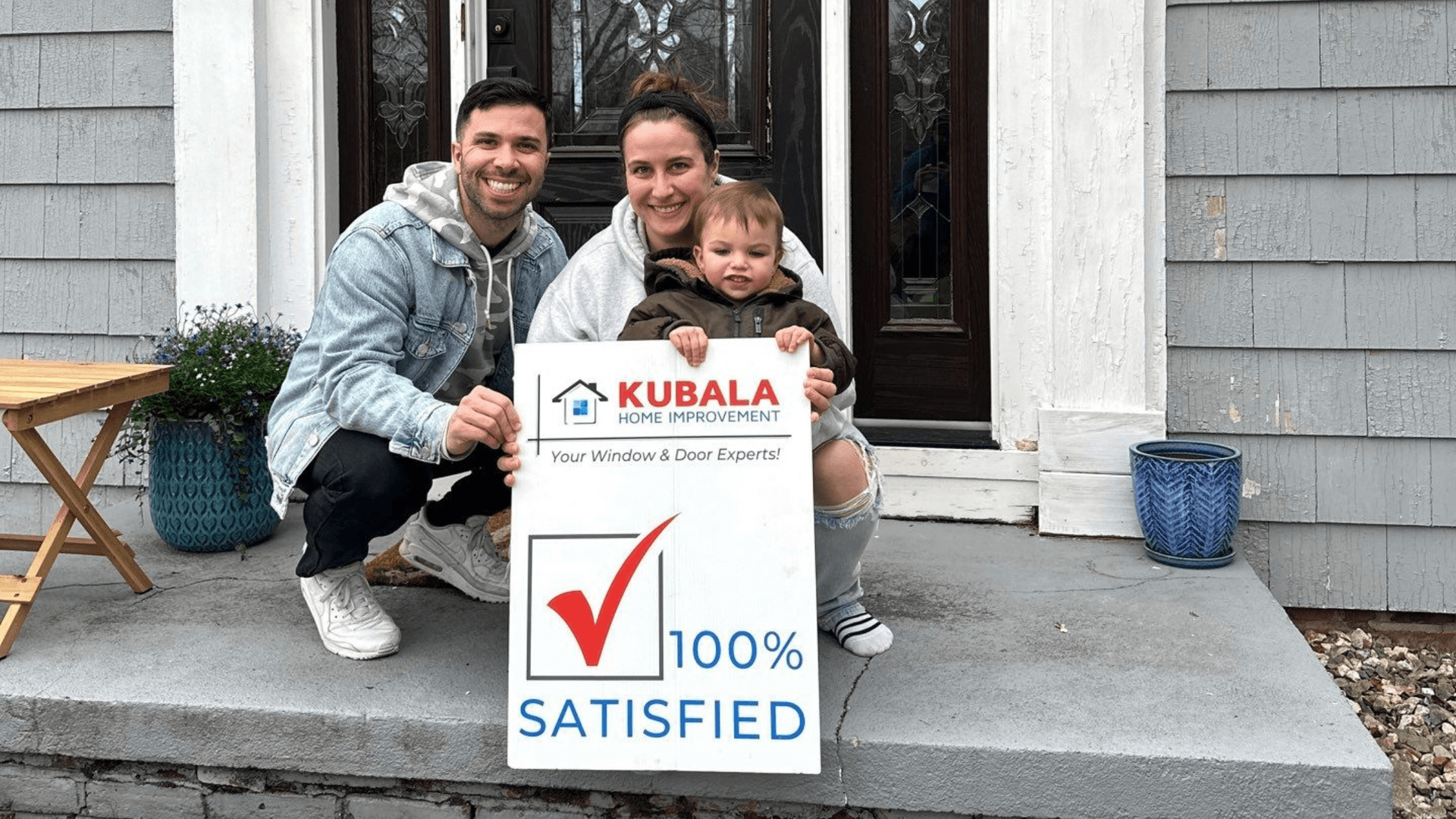 Picture of homeowners and their child smiling and holding a "100% Satisfied" sign in front of their new windows in Springfield, MA.